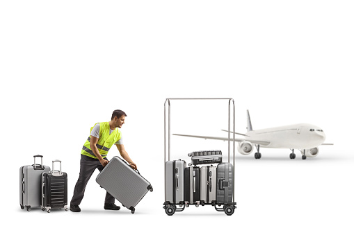 Airport worker putting suitcases on a luggage trolley in front of an aircraft isolated on white background