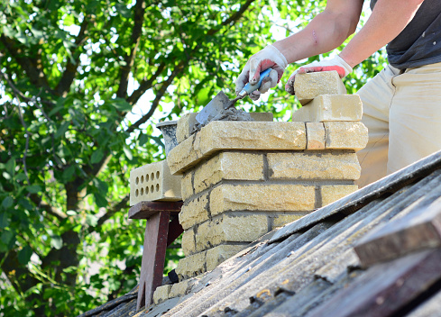 Repairing a brick chimney with bricklaying.  Building contractor is rebuidling a chimney on a house with asbestos roof.