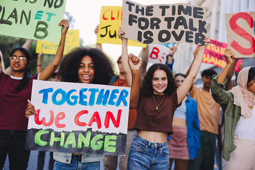 Youth protest against climate change. Group of multicultural youth activists carrying posters and banners while marching against global warming. Happy young people joining the global climate strike.