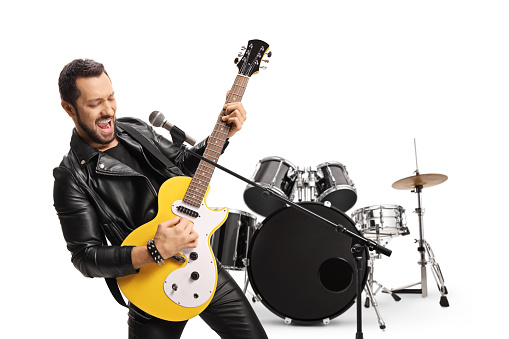 Rocker guitarist playing an electric guitar in front of a drum set isolated on white background