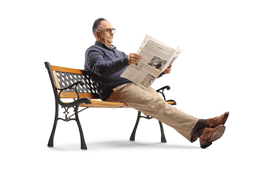 Mature man sitting on bench and reading a newspaper isolated on white background