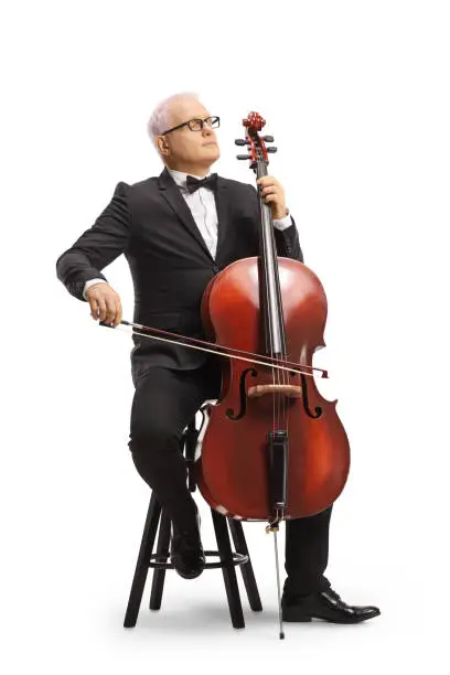 Full length portrait of a musician in a black suit and bow-tie sitting on a chair and playing a cello isolated on white background