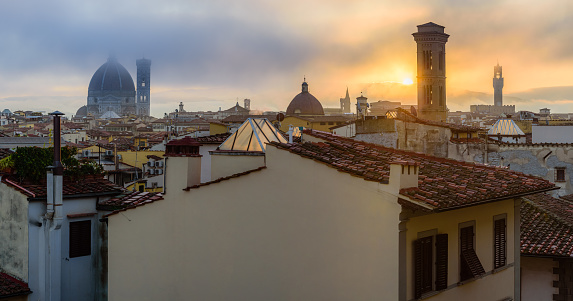The rising sun over the Florence cityscape with the towers of the Duomo, Chiesa di San Salvatore in Ognissanti and the Palazzo Vecchio in the fogy autumn morning.