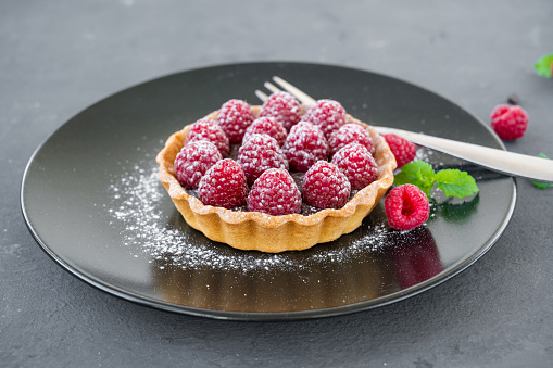 Delicious chocolate tart with raspberry on the plate on a gray background. Summer dessert. Copy space.