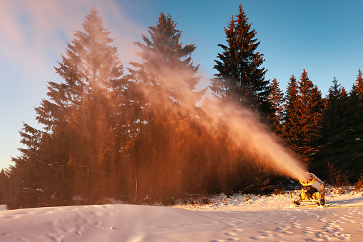 Snow cannon in winter mountains. Snow-gun spraying artificial ice crystals. Machine making snow.