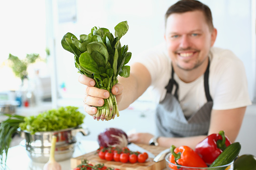 Smiling male cook holding sorrel or salad in kitchen. Healthy ways to cook vegetables concept