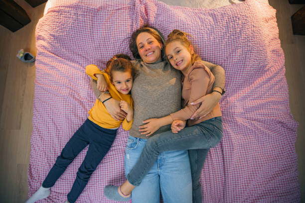 istock mother and daughters in bed smiling and cuddling, looking at the camera high angle shot 1457332825