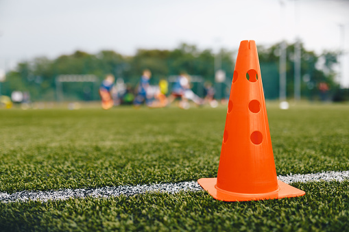 Plastic training cone on the football pitch. Soccer training equipment on an artificial grass field. Red practice cone standing on the sideline