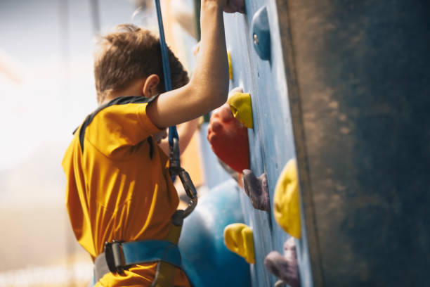 Little boy climbing a rock wall indoor. Bouldering training class for school kids