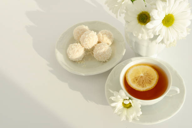 Tea, sweets and white flowers on a white table, top view
