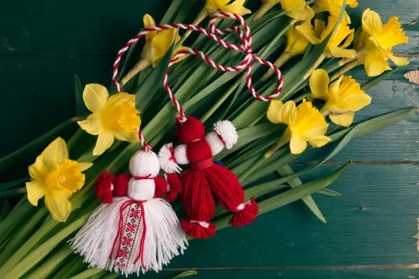 Martenitsa, Martisor on a bouquet of yellow daffodils on a green wooden table top view close up