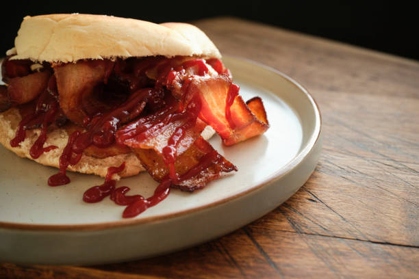 istock Breakfast bun, soft white roll filled with rashers of smoked bacon covered in tomato ketchup. 1457340465