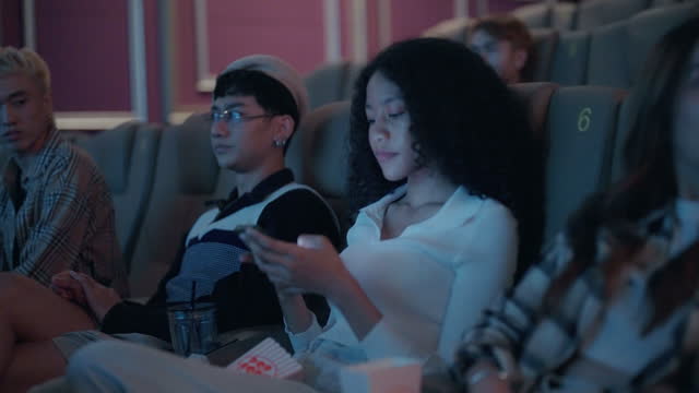 Asian woman is using her smartphone to text and chat with her friend in the cinema.
