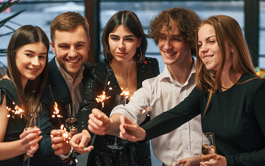 With new year sparklers. Group of people in beautiful elegant clothes are indoors together.