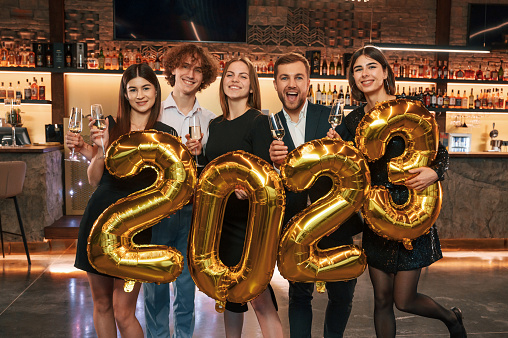 With 2023 numbers balloons. Group of people in beautiful elegant clothes are celebrating New Year indoors together.