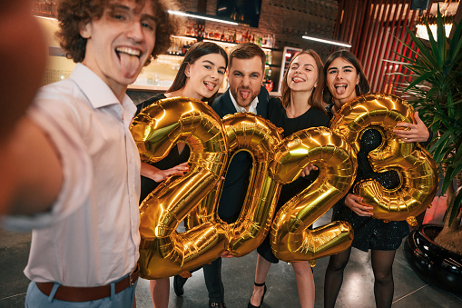 2023 is coming. With balloons. Group of people in beautiful elegant clothes are celebrating New Year indoors together.