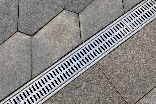 The grid of the rainwater drainage system on the sidewalk made of stone paving slabs. Top view