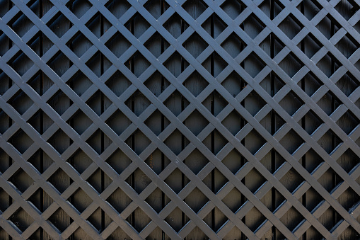 A fragment of a wooden fence made of painted black boards. Wooden diagonal lattice. Copy space.