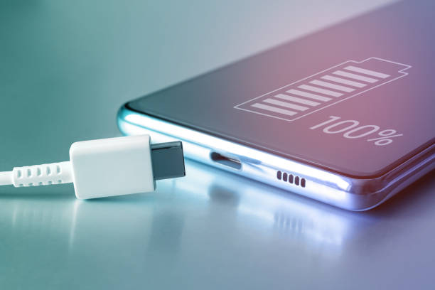 Fully charged battery icon on the touch screen of the cell phone and a USB Type-C cable. Fully charged smartphone battery. Keeping the battery intact. Battery safety