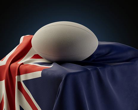 A regular rugby ball resting on a New Zealand flag draped over a plinth on an isolated studio background - 3D render