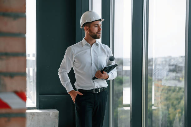 istock Standing near panoramic windows. Man in white shirt is working indoors at construction site. Managing the project 1457348070