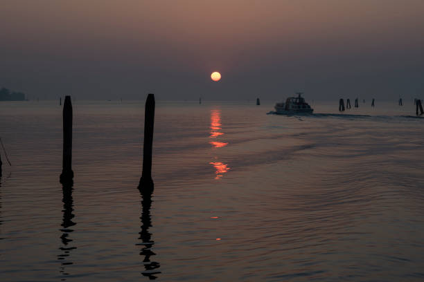 The sun sets over the water in Venice, with a boat leaving a wake.