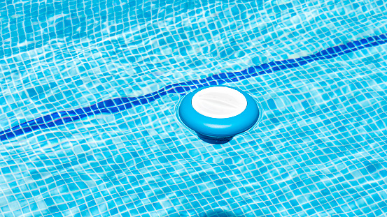 Floating dispenser in the pool with a chlorine tablet inside to correct the ph of the water before swimming. Blue and white chemical dosing float for chlorine tablets