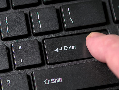 A person's hand pressing the Enter key on a black computer keyboard. Close up, macro shot