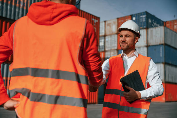 istock Making handshake. Two male workers is on the location with containers 1457353618