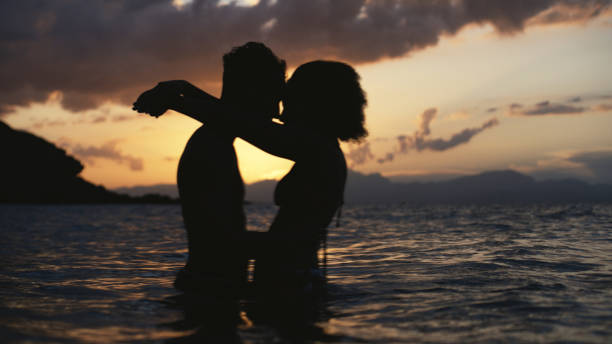 African ethnicity romantic heterosexual couple swimming and embracing in the sea at dusk together stock photo