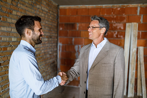 Happy man shaking hands with an investor after reaching an agreement at construction site. Copy space.