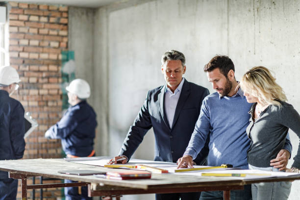 istock Young couple and their agent examining blueprints at construction site. 1457355914
