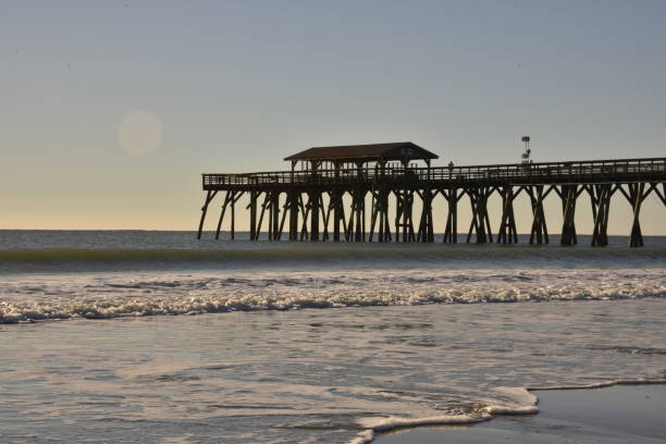 istock Silhouetted Pier Against Waves On The Beach 1457358519