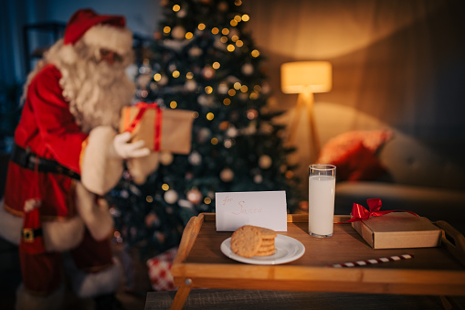 Santa Claus bringing Christmas presents, cookies and glass of milk that is left for him on a tray at home.
