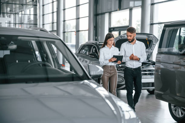 Walking forward and talking. Man with woman in white clothes are in the car dealership together stock photo