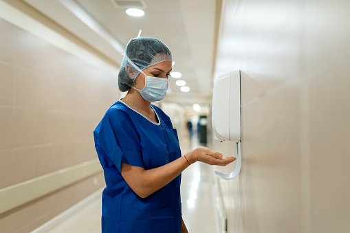 A female doctor putting sterilizing gel on her hands in a hospital corridor