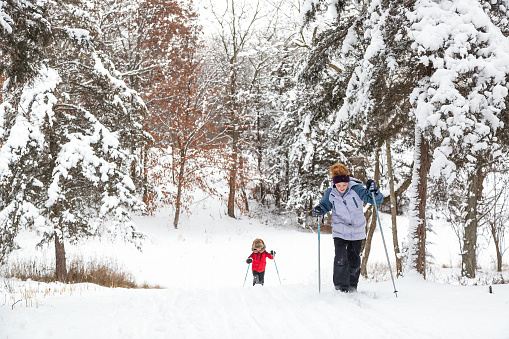 Front view of two children cross country skiing up a hill on a snowy winter day.