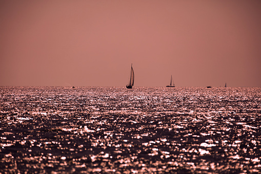 Silhouette of a sailing boat in sunset sunrise time and ocean horizon.