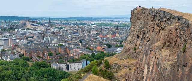 Edinburgh,Scotland-August 01 2022: Visitors climbing to the iconic summit,stand at the precipice of a giant vertical cliff,in awe of views across Edinburgh,on a summer day in Scotland's capital.