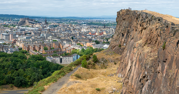 Edinburgh,Scotland-August 01 2022: Visitors climbing to the iconic summit,stand at the precipice of a giant vertical cliff,in awe of views across Edinburgh,on a summer day in Scotland's capital.