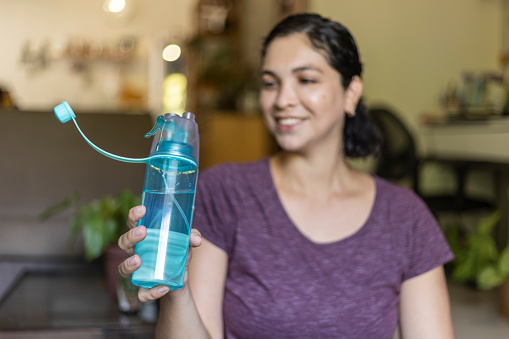 Latin woman drinking water from a bottle after yoga exercise