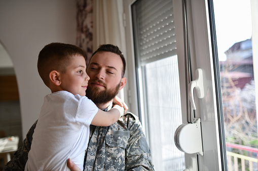Small Boy Embracing Soldier Father While Relaxing Together At Home