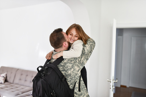 military father in camouflage clothing hugging his son at home - war concept -
