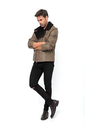 Handsome middle-aged hispanic stubby bearded man on white studio. Short-haired handsome man in leather jacket, t-shirt and jeans, on white background. Spanish middle-aged man in autumn clothes crossing his arms and head bowed thoughtfully.