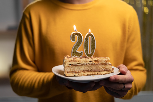 Cake with the number 20 lighted candles in men hands. 20th birthday concept