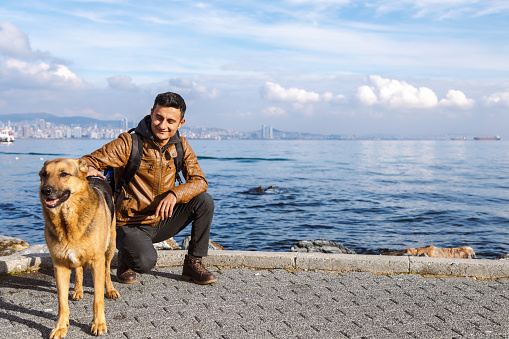 Smiling asian man petting stray dog on near water shore