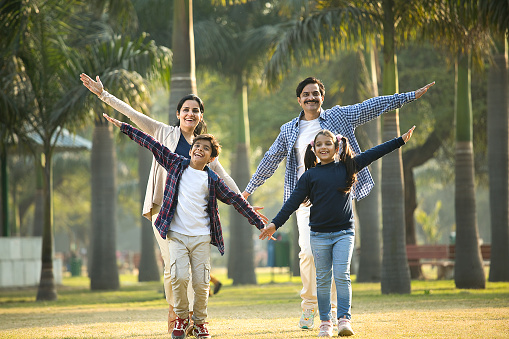 Portrait of cheerful two generation family with arms outstretched at park