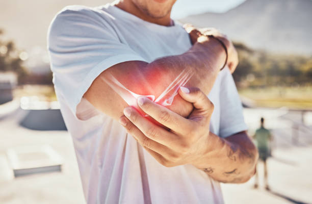 Man, joint pain and elbow arthritis in outdoor closeup in summer sunshine with massage arms. Broken arm, bone and guy at urban park in metro, city or town with physical therapy with hands in zoom stock photo