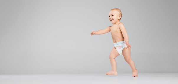 Full-length footage of cute toddler boy, baby in diaper isolated over grey studio background. Concept of happy childhood, motherhood, life, birth and health. Banner with copy space for ad