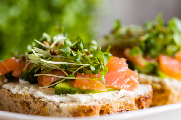 Two open sandwich, toast with salmon, cream cheese, avocado, cucumber slices on white concrete table. Morning healthy breakfast with fish, side view, copy space. Selective focus. Healsy food concept. dos sándwiches abiertos, tostadas con salmón, queso crema, aguacate, rodajas de pepino sobre mesa de concreto blanco. desayuno saludable por la mañana con pescado, vista lateral, espacio de copia. enfoque selectivo. concepto de comida curativa.
